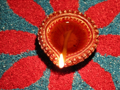 Author: nkjain via Wikipedia Commons रंगबिरंगी रंगोली पर सजा, तेल का जलता हुआ दीया। Burning oil lamp on a colourful rangoli designed on Diwali.